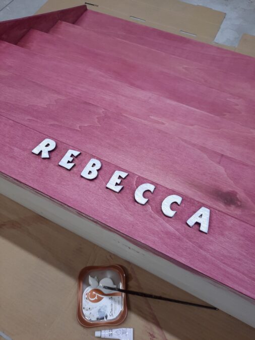 The letters painted white on the pink Montessori bookshelf