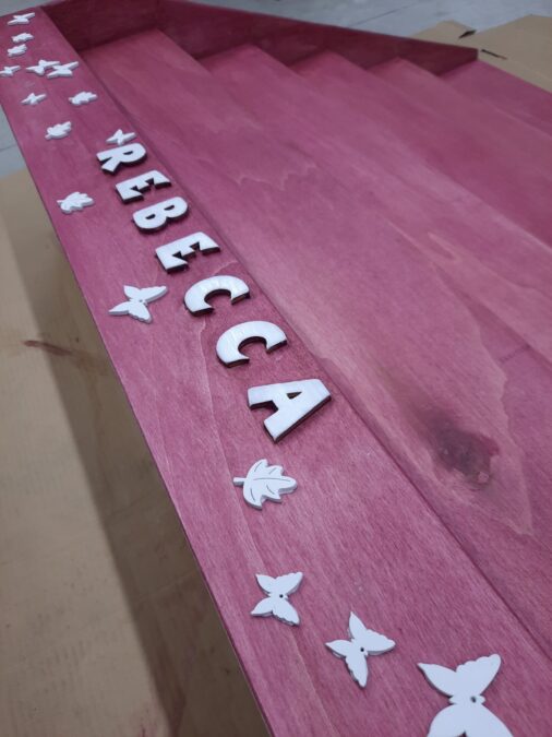 The Montessori bookshelf is painted pink and decorated with white letters, leaves and butterflies