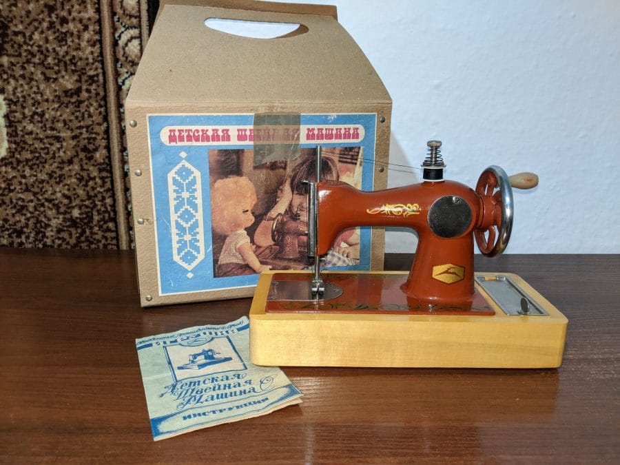 An Orsha sewing machine with its original cardboard box and manual. On the box, in Russian, "ДЕТСКАЯ ШВЕЙНАЯ МАШИНА" ("Children's Sewing Machine")